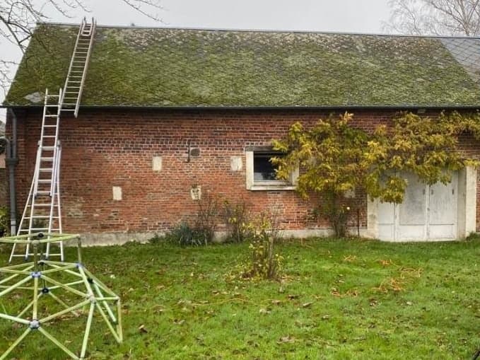 Grange en brique dont la couverture est couverte de mousse verte